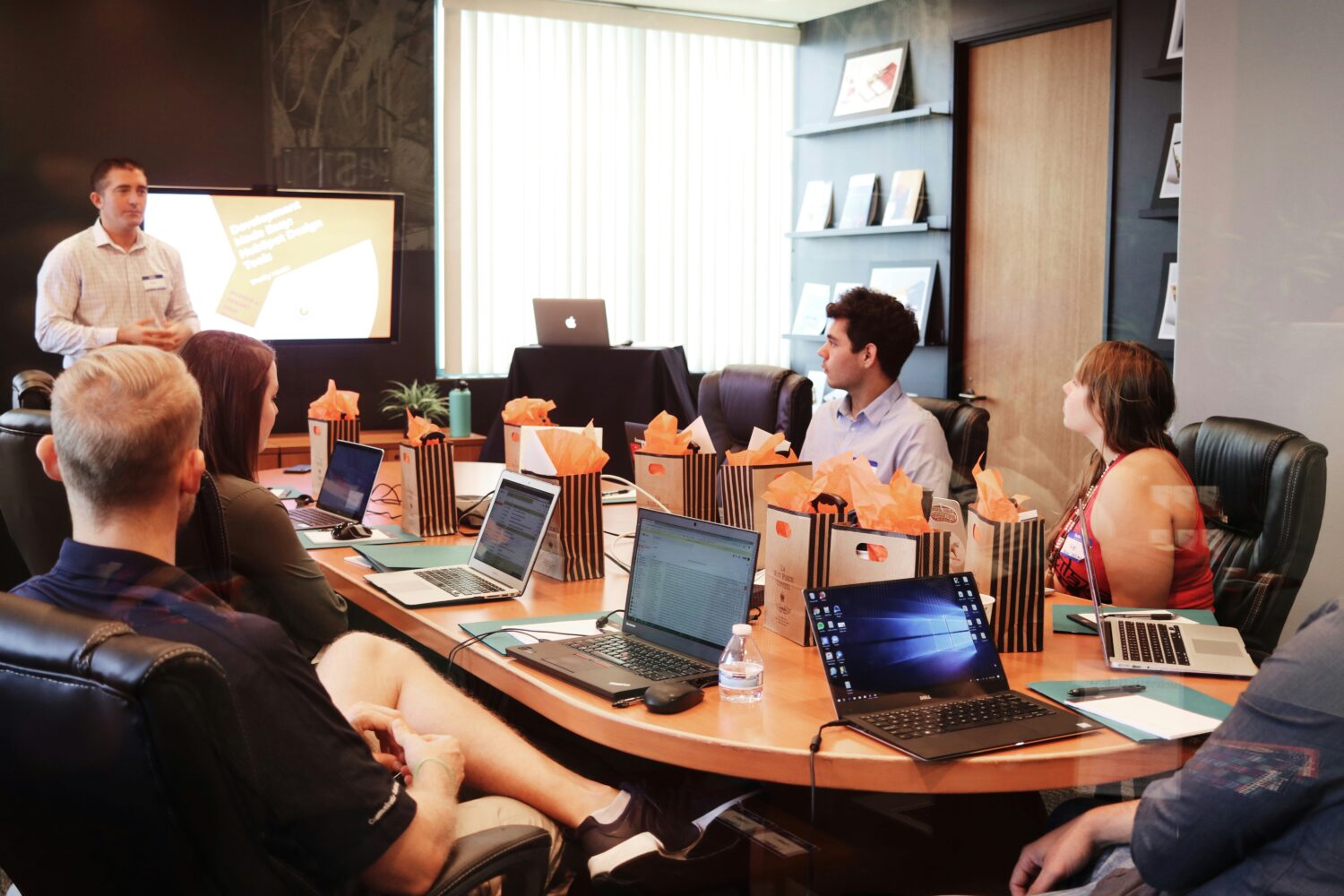 A conference room filled with people with laptops on desk listening to the speaker in front