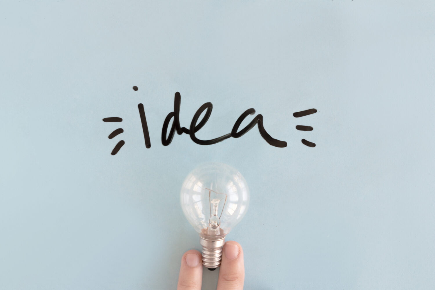 close up person's hand holding a light bulb near black idea word 