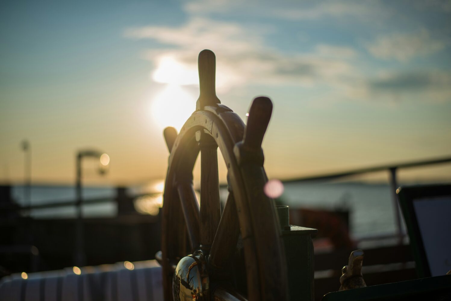 brown wooden ships wheel with a reflection of the sunset